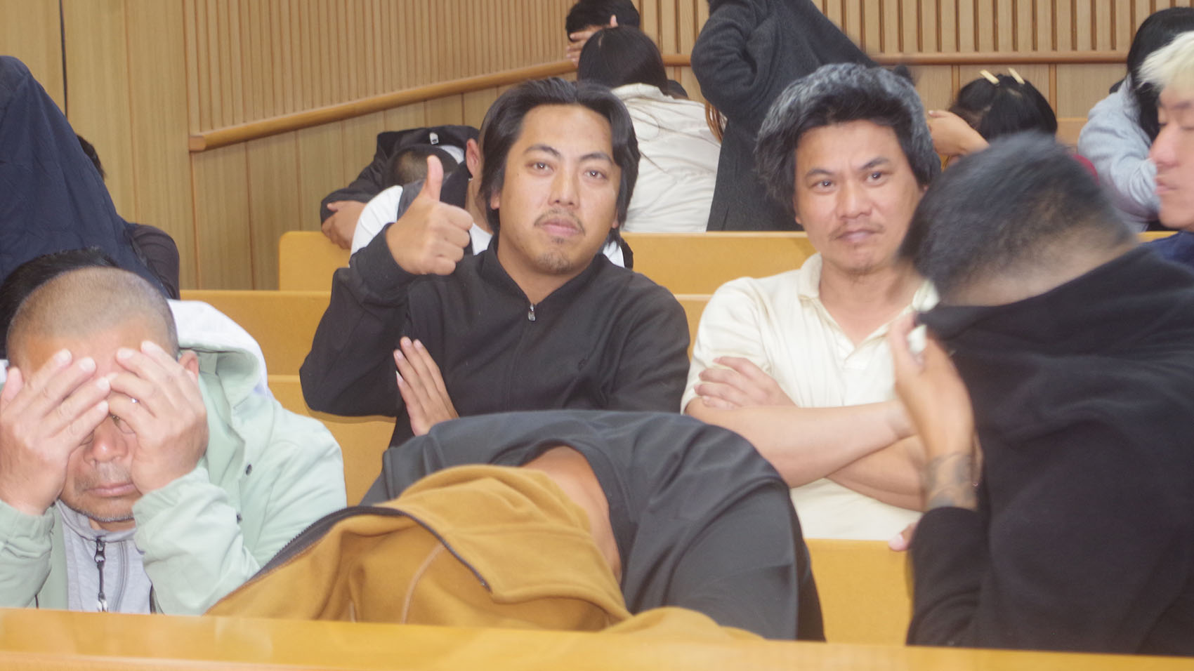 One of the accused reacts to the camera while his co-accused hide their faces. 